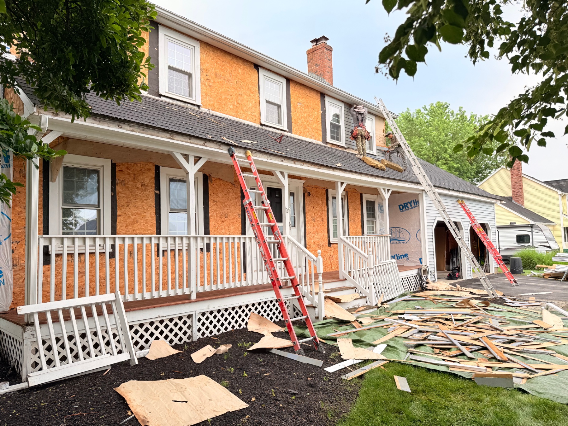 Crew stripping old cedar clapboard siding with exposed sheathing and ladders